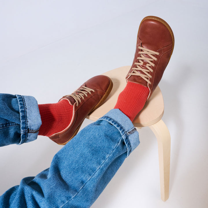 Zapatillas barefoot de cuero Origo Everyday Sneaker Cinnamon, puestas con jeans y calcetines rojos, sentado